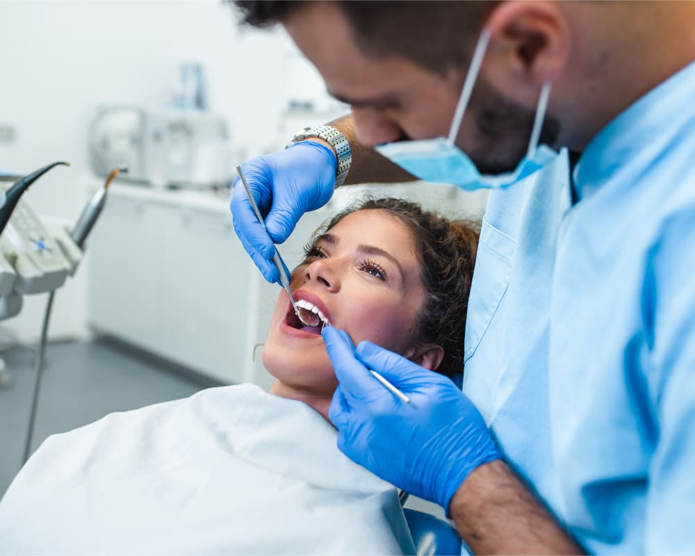 A male dental professional is working on a female patient's mouth.